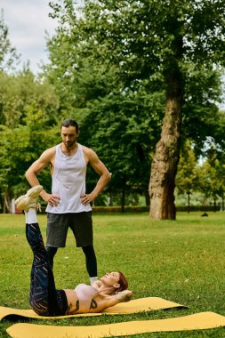 Spor giyimli bir kadın, özel antrenör tarafından yönlendirilmiş, yoga pozisyonunda kararlı ve motivasyonlu bir şekilde huzurlu bir parkta poz veriyor..