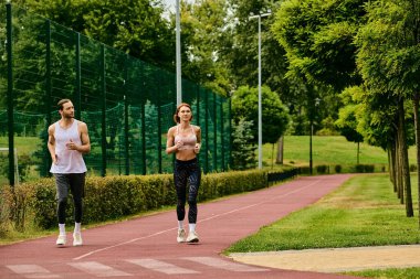 Spor giyimli bir çift, enerjik bir şekilde bir yolda koşuyorlar, azim ve motivasyon gösteriyorlar..