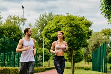 Spor giyimli bir kadın ve erkek, parkta birlikte koşuyorlar, azim ve motivasyondan besleniyorlar.