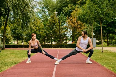 determined woman and man in sportswear stretching, showing dedication to their outdoor workout. clipart