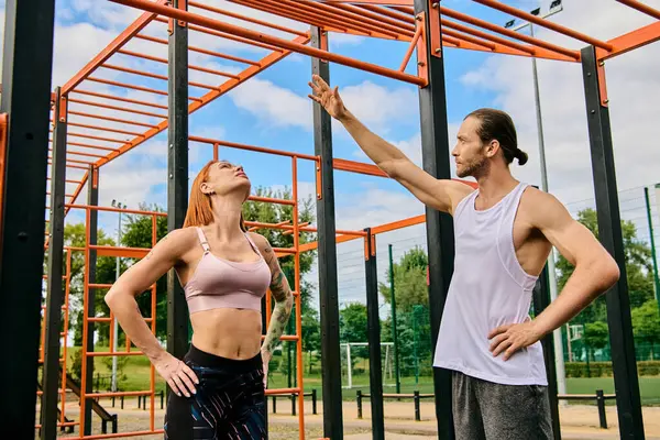 Spor giyim sektöründe bir erkek ve bir kadın, metal bir yapının önünde durur. Açık hava idmanı sırasında azim ve motivasyon gösterirler..