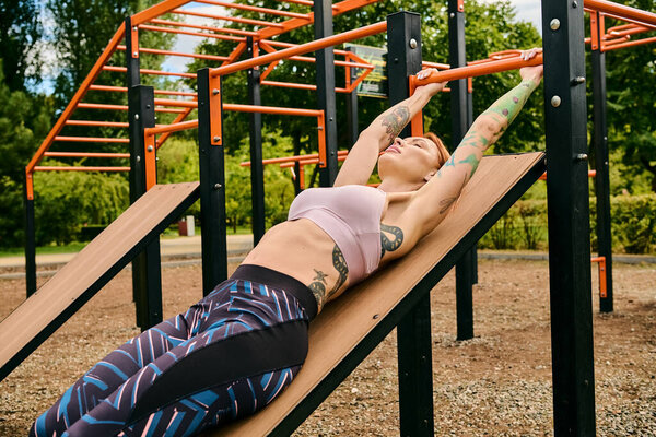 A woman in sportswear lies peacefully on a wooden bench during a workout session outdoors.