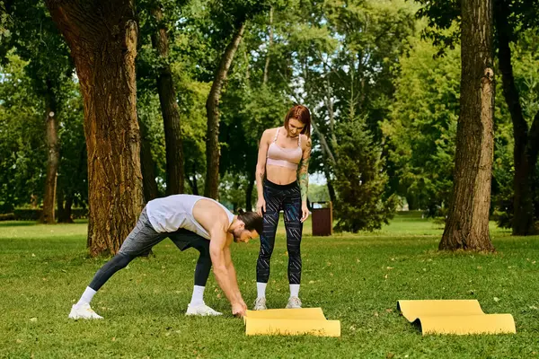 Spor kıyafetleri giymiş bir çift yoga pozisyonları serin bir park ortamında kişisel antrenör rehberliği yapıyor..