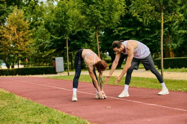 A determined woman in sportswear, guided by a personal trainer, are exercising together on a track. clipart