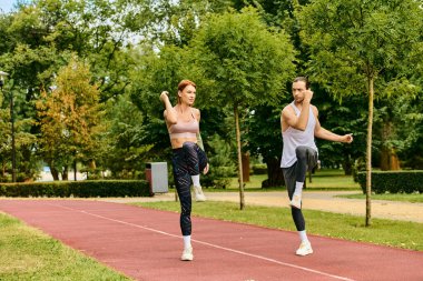 A determined man and woman, dressed in sportswear, are stretching together on a track clipart