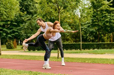 Spor giyimli bir kadın çimlerin üzerinde duruyor, kişisel antrenörüyle açık hava fitness antrenmanına katılıyor..