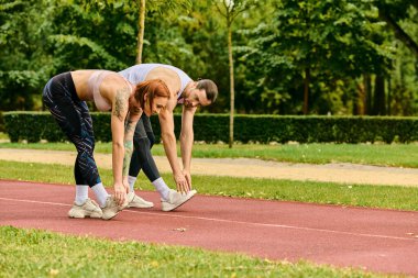 Spor kıyafetleri giymiş bir erkek ve kadın, bir pistte birlikte antrenman yapıyorlar, azim ve motivasyon gösteriyorlar..