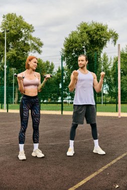 Spor giyimli kararlı bir erkek ve kadın halterlerle dışarıda egzersiz yapıyor.