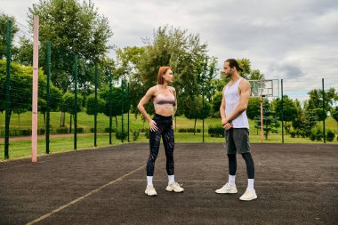 Spor kıyafetleri giyen bir erkek ve kadın, basketbol sahasında durup, açık hava egzersizleri sırasında azim ve motivasyon gösteriyorlar..