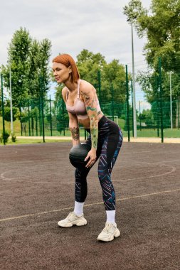 Spor giyimli bir kadın, elinde bir tıp topu tutuyor, açık havada azim ve motivasyonla antrenman yapıyor.