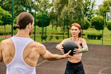 Kararlı bir kadın spor giyimli bir adamın yanında durup egzersiz yapmaya olan bağlılığını gösterirken topu tutuyor..
