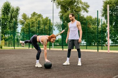 A woman in sportswear enjoy a playful moment, exercising outdoors with a ball under the guidance of a personal trainer. clipart