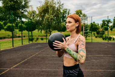 Spor giyimli bir kadın, tıp topu tutuyor, dışarıda azim ve motivasyonla antrenman yapıyor.