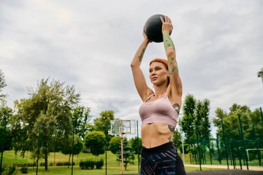 Spor kıyafetli bir kadın, elinde bir sağlık topu tutuyor, dışarıda motivasyonla antrenman yapıyor.