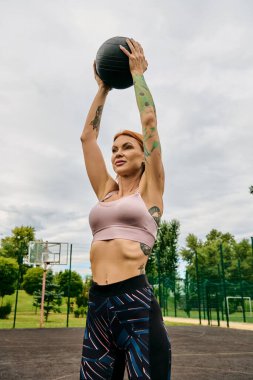 Spor kıyafetli bir kadın, elinde sağlık topu, dışarıda antrenman yapıyor.
