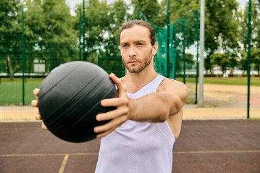 Spor kıyafetli bir adam sahada duruyor, elinde bir tıp topu tutuyor..