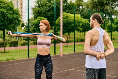 Spor giyimli bir kadın, kişisel antrenör tarafından yönlendiriliyor, bir kortta tutkuyla egzersiz yapıyor, azim ve motivasyon gösteriyor..