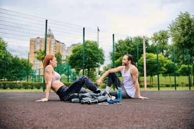 Kendini adamış bir özel antrenör, motivasyonlu bir erkek ve kadına spor giysileri ile açık havada egzersiz yaptırır..
