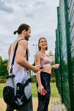 A determined man and woman in sportswear stand alongside a fence after workout clipart