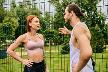 A determined woman talks with a personal trainer while exercising in front of a fence outdoors. clipart