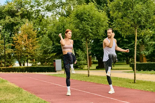 A determined man and woman, dressed in sportswear, are stretching together on a track
