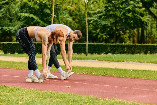 Spor kıyafetleri giymiş bir erkek ve kadın, bir pistte birlikte antrenman yapıyorlar, azim ve motivasyon gösteriyorlar..