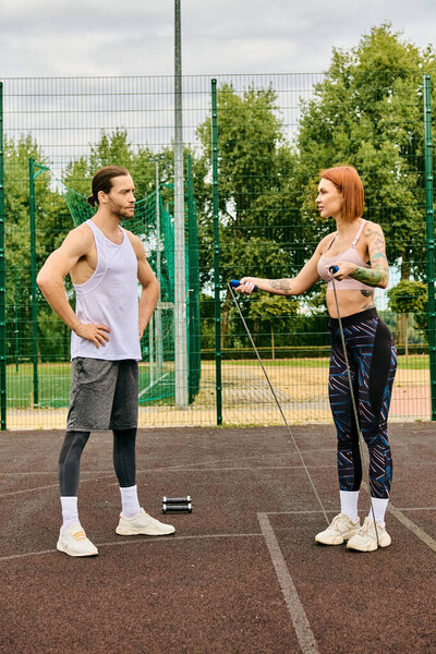 A woman in sportswear and her personal trainer, are standing on a tennis court, determined and motivated to exercise together.