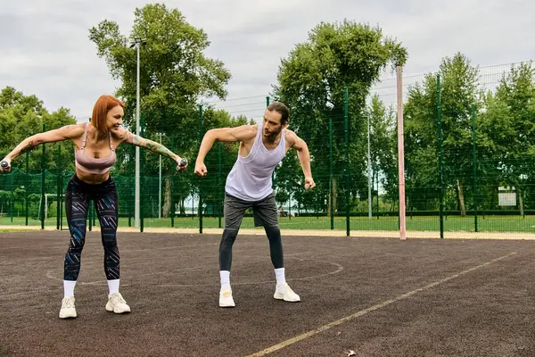 Spor kıyafetleri giymiş kararlı bir erkek ve kadın halterlerle birlikte dışarıda egzersiz yapıyorlar.