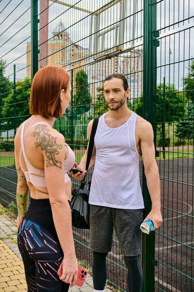 A determined man and woman in sportswear stand together outdoors by a fence,
