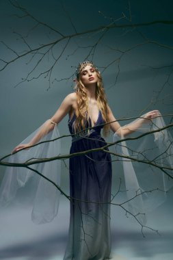 Mavi elbiseli genç bir kadın geniş bir ağaç dalının önünde zarif bir şekilde duruyor. Tuhaf bir stüdyo ortamında..