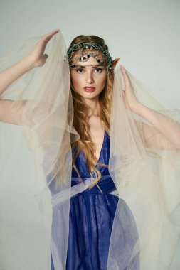 Genç bir kadın, mavi bir elbiseyle zarif bir duvak takıyor. Kafasının üstünde, gizemli bir peri prensesinin özünü simgeliyor..