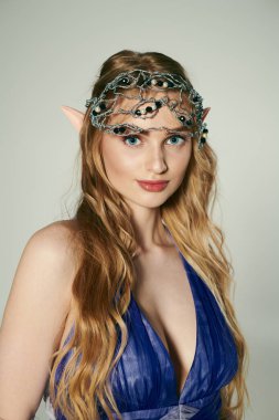 Kafasında taç olan mavi elbiseli genç bir kadın mistik bir stüdyo ortamında bir peri prensesin özünü somutlaştırıyor..