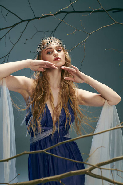 Молодая женщина в синем платье грациозно стоит перед величественным деревом в студии, воплощая принцессу эльфов.