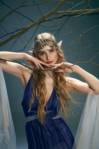 Молодая женщина в синем платье стоит, держа деликатный филиал в студии, воплощая сказочного персонажа.