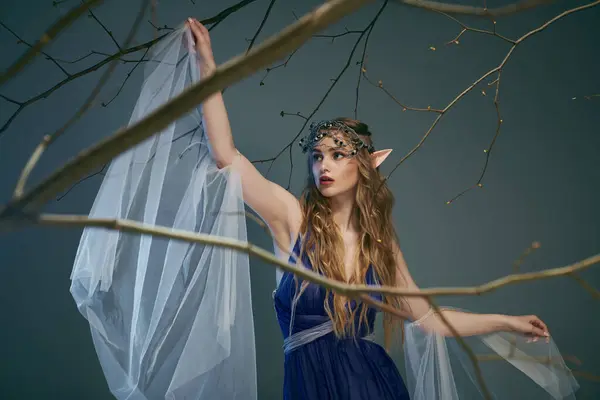 青いドレスの若い女性は優雅にエルフの王女に合う魔法のスタジオの設定で繊細な白いベールを保持しています — ストック写真