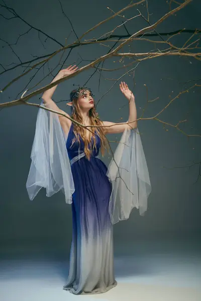 一个身穿蓝白相间衣服的年轻女子拿着一根纤细的枝条 在异想天开的环境中象征着一位仙女公主 — 图库照片