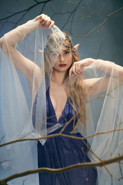 A young woman exudes ethereal beauty in a blue dress and a veil, embodying the essence of a fairy-tale princess in a studio setting.