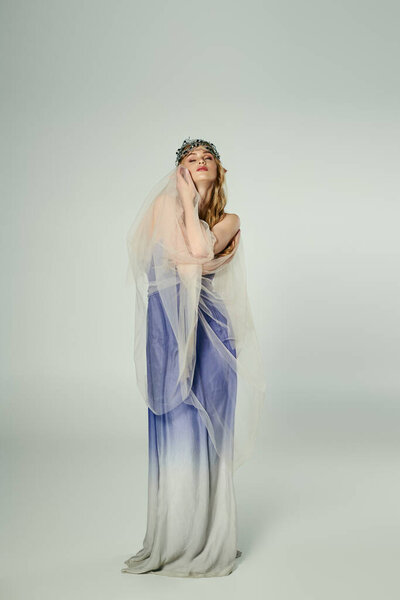 A young woman dressed in a blue and white gown with a flowing veil, embodying the essence of a fairy princess in a studio setting.