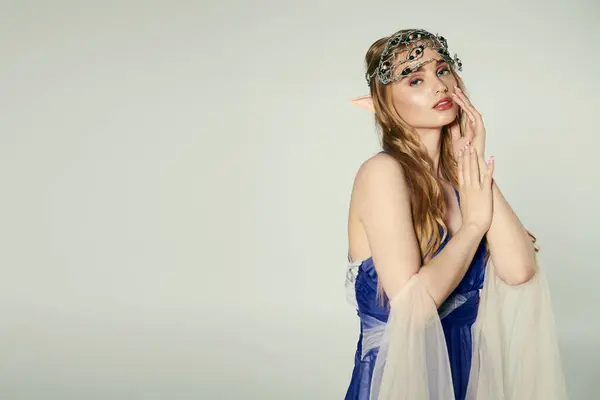 stock image A young woman embodies an elf princess in a blue dress with a delicate veil in a whimsical studio setting.