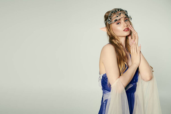 A young woman embodies an elf princess in a blue dress with a delicate veil in a whimsical studio setting.