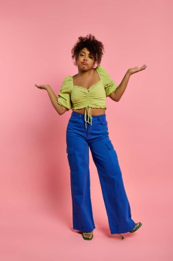 Sarı bluzlu ve mavi pantolonlu şık Afro-Amerikan kadın canlı arka planda poz veriyor..