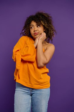 Emotional African American woman in stylish orange shirt strikes a pose against a vibrant backdrop. clipart
