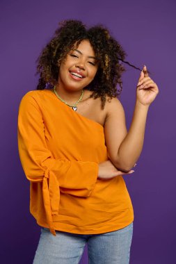 Stylish African American woman in orange top touching her hair. clipart