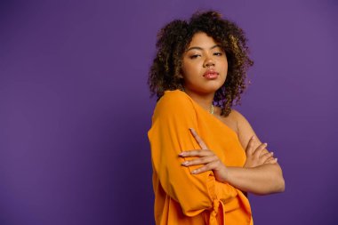 Afro-Amerikalı şık bir kadın canlı turuncu bir bluzla poz veriyor..