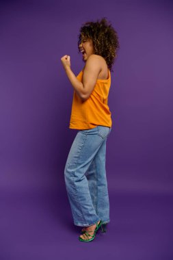 Stylish woman posing in yellow shirt and blue jeans against vibrant backdrop. clipart