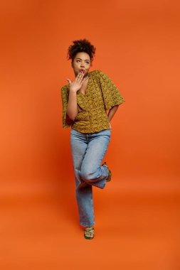 Canlı turuncu arkaplan önünde poz veren şık Afrikalı Amerikalı kadın.