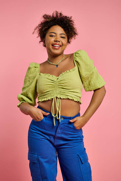 Stylish African American woman posing in yellow top and blue pants on a vibrant backdrop.