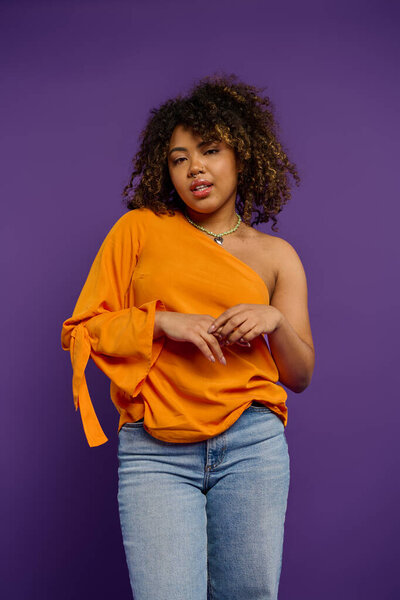 A beautiful African American woman in an orange top striking a pose against a vibrant backdrop.