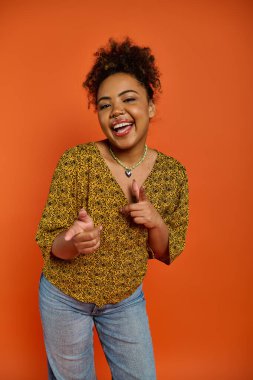 Sarı gömlek ve kot pantolon içinde canlı poz veren şık Afrikalı Amerikalı kadın..