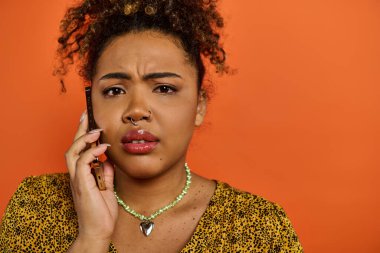 Afro-Amerikan kadın şık giyinmiş, kulağına cep telefonu dayamış..